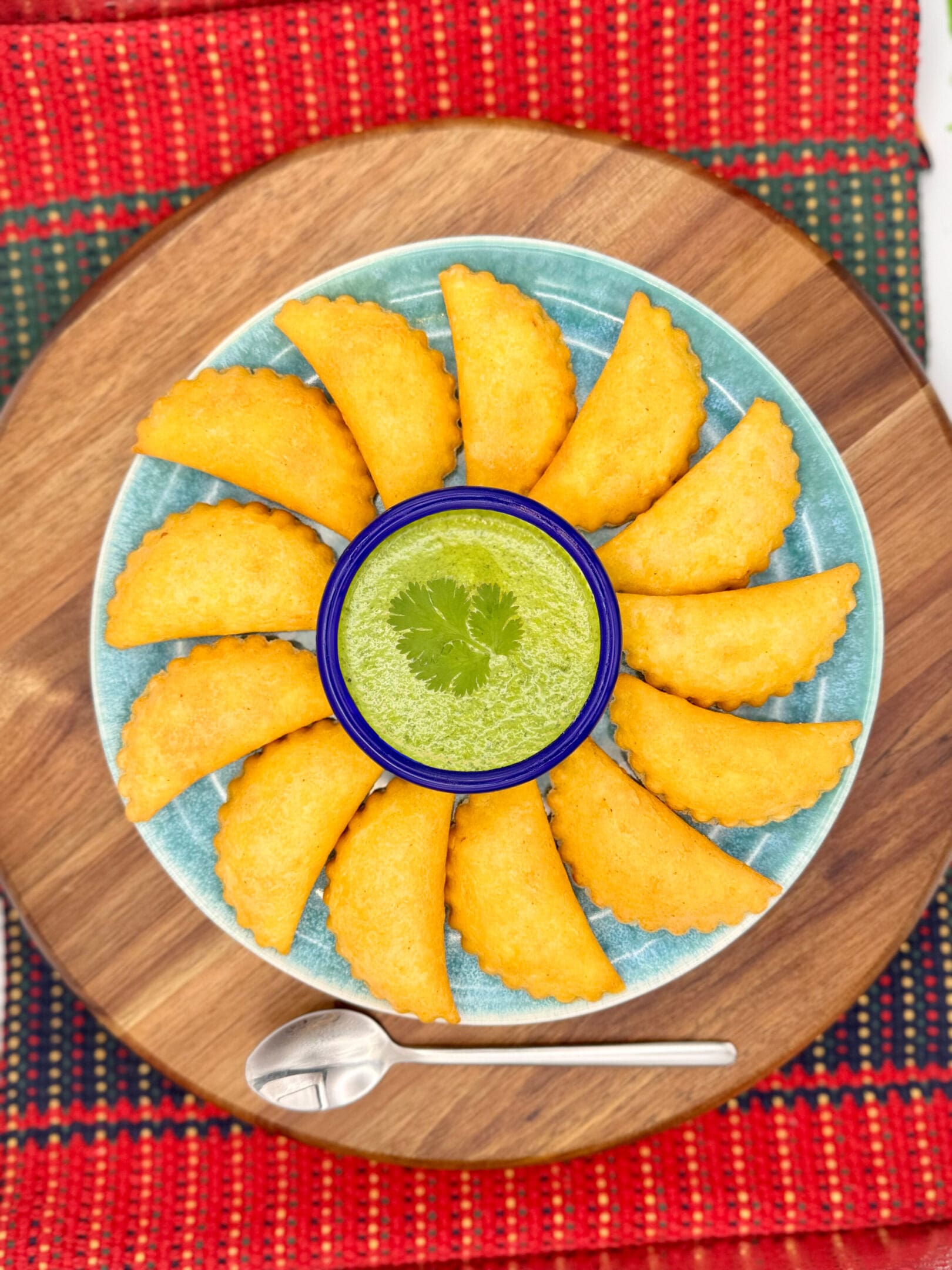 Golden fried empanadas arranged in a circle with green chutney dip in the center.