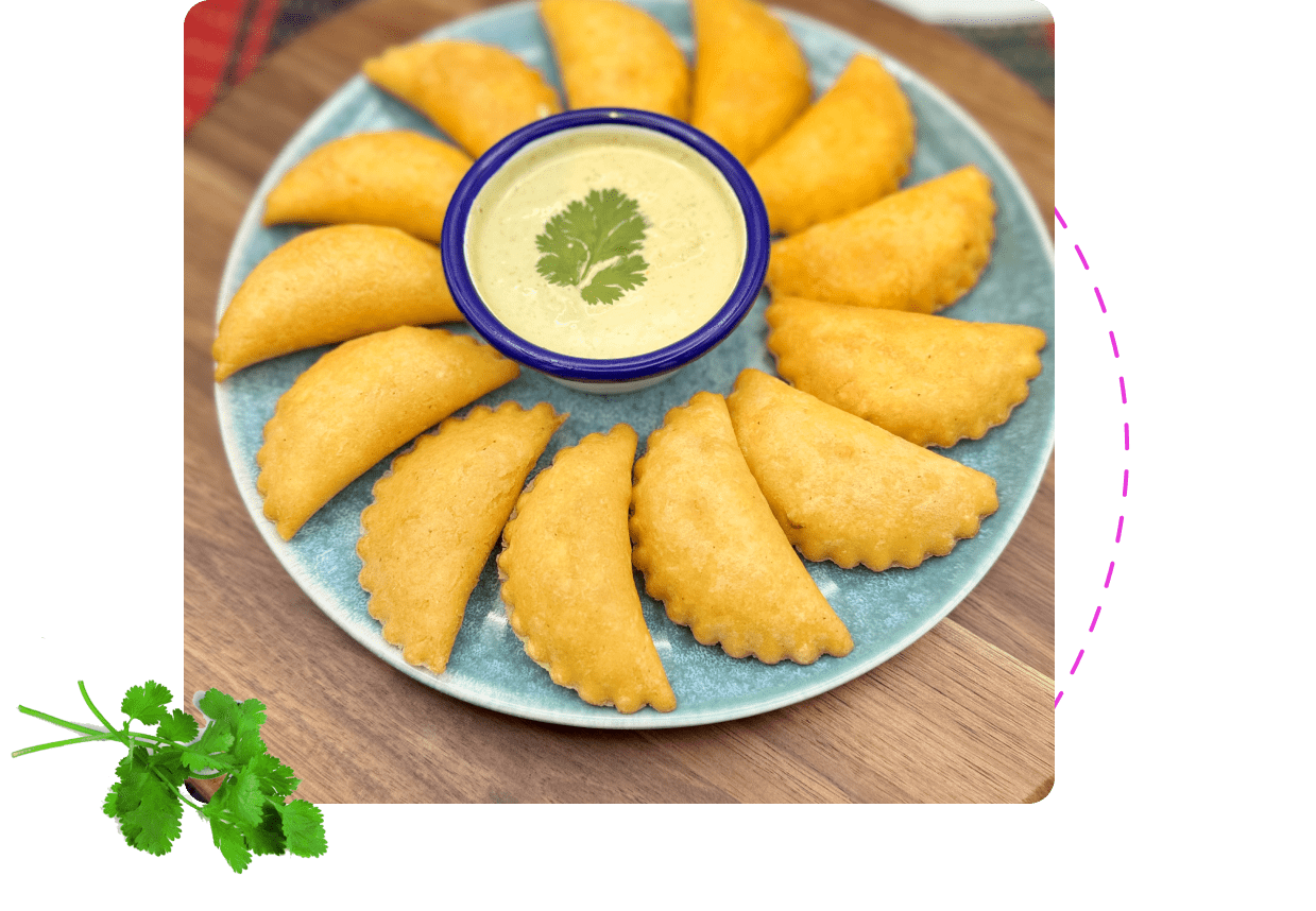 A platter of corn empanadas with a garlic salsa