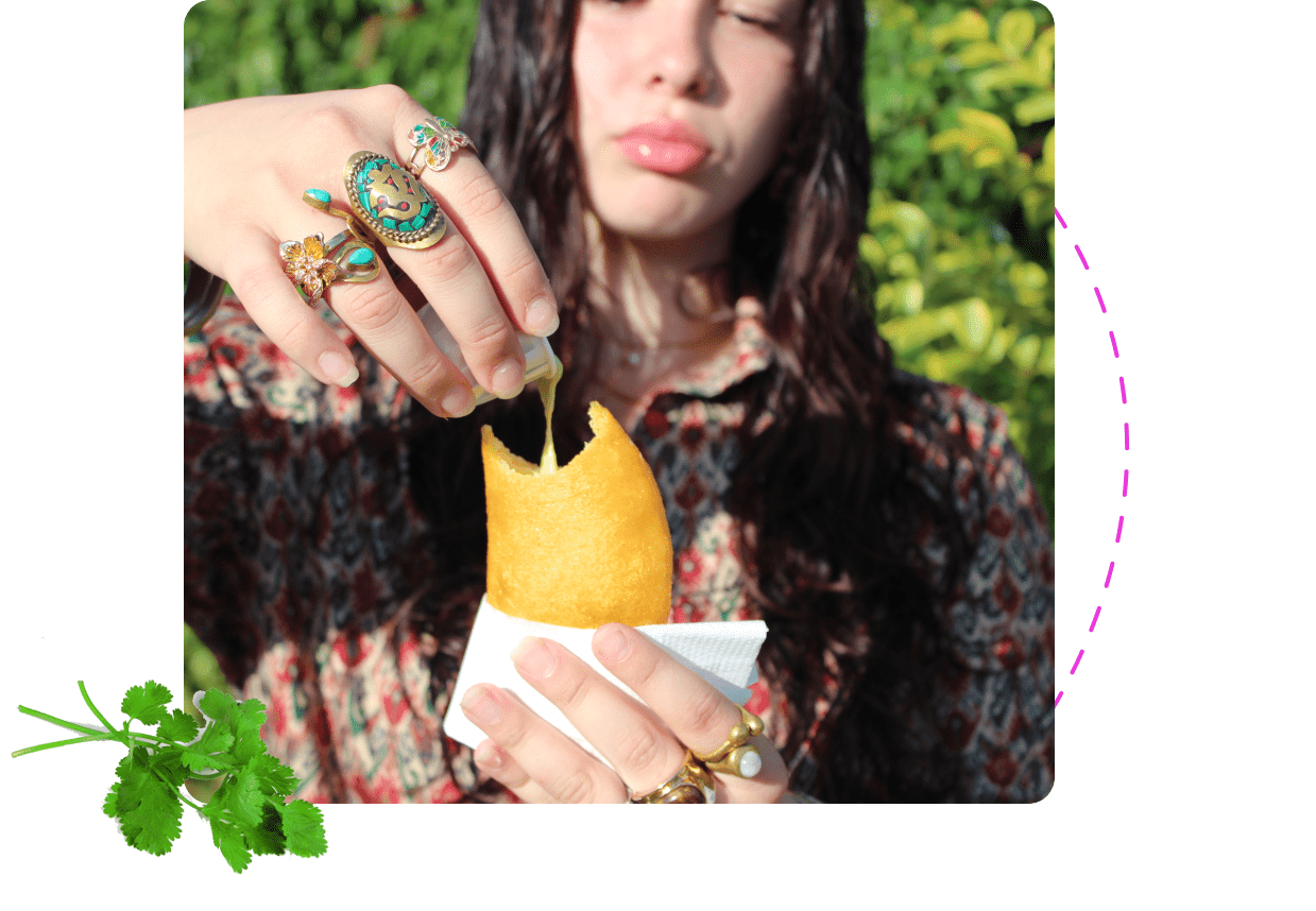 Person drizzling sauce over golden empanada held in hand outdoors