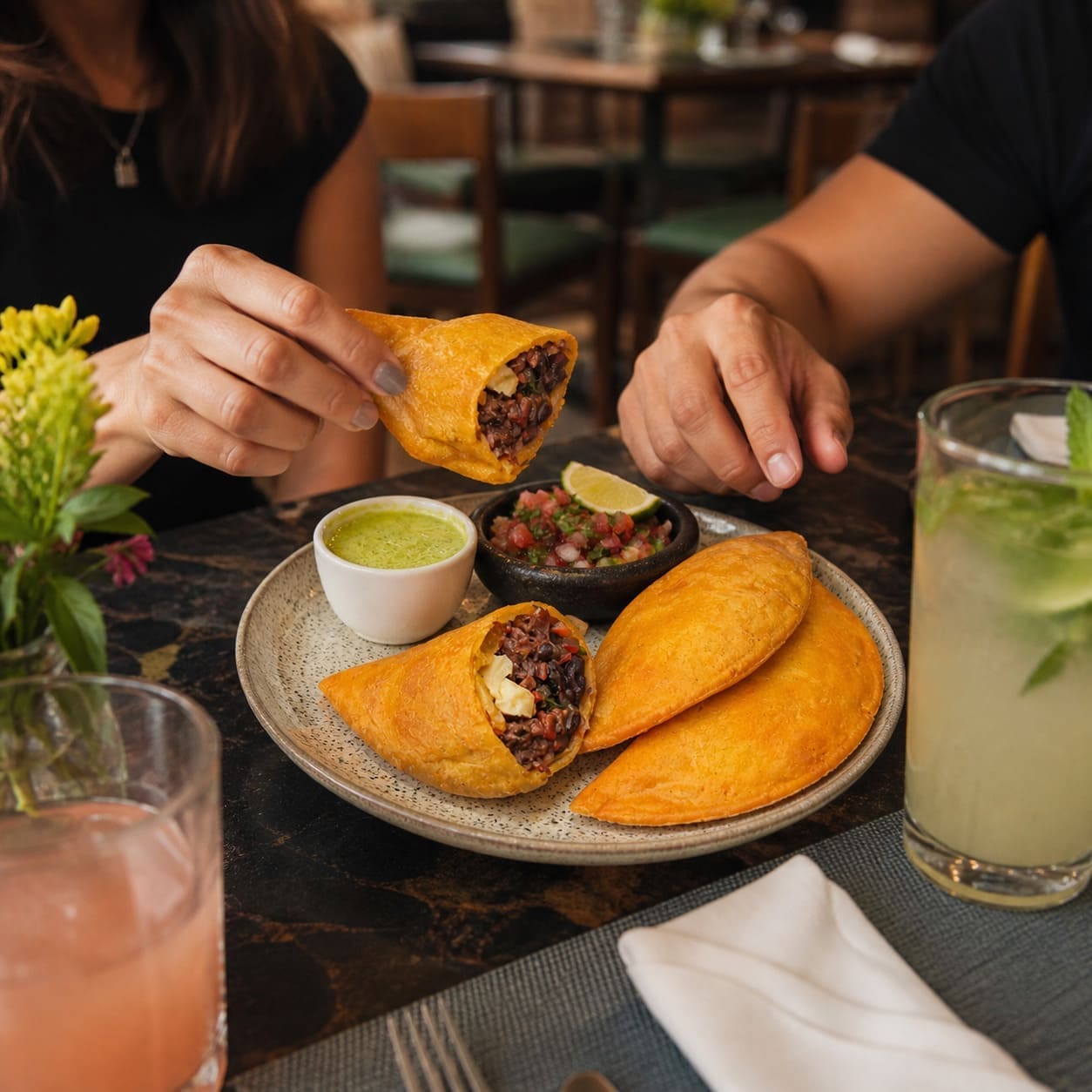 Hands reaching for plated golden empanadas with shredded beef, plantain and cheese – Illustrative Image