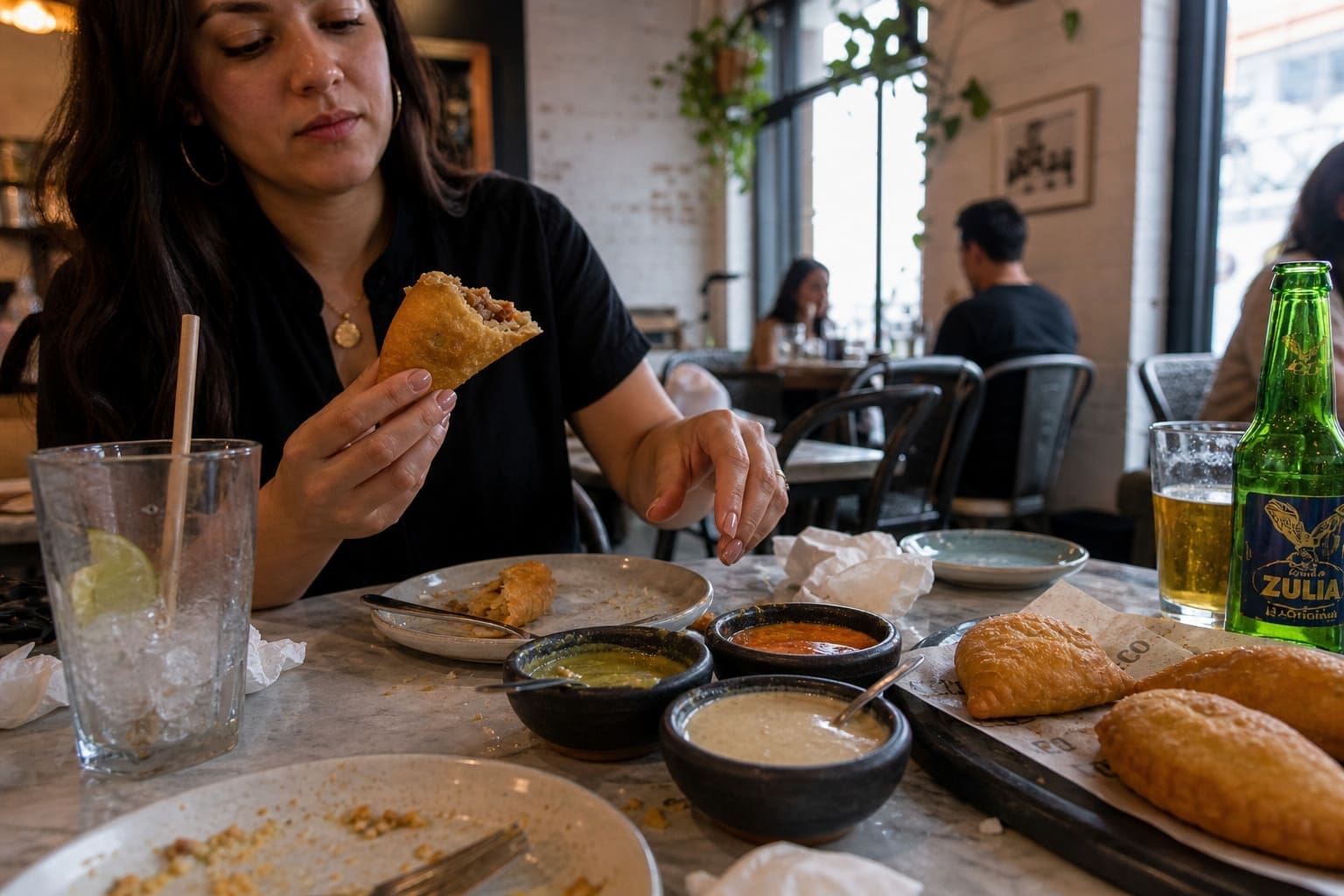 Woman enjoying a golden empanada with dipping sauces at cafe – Illustrative Image