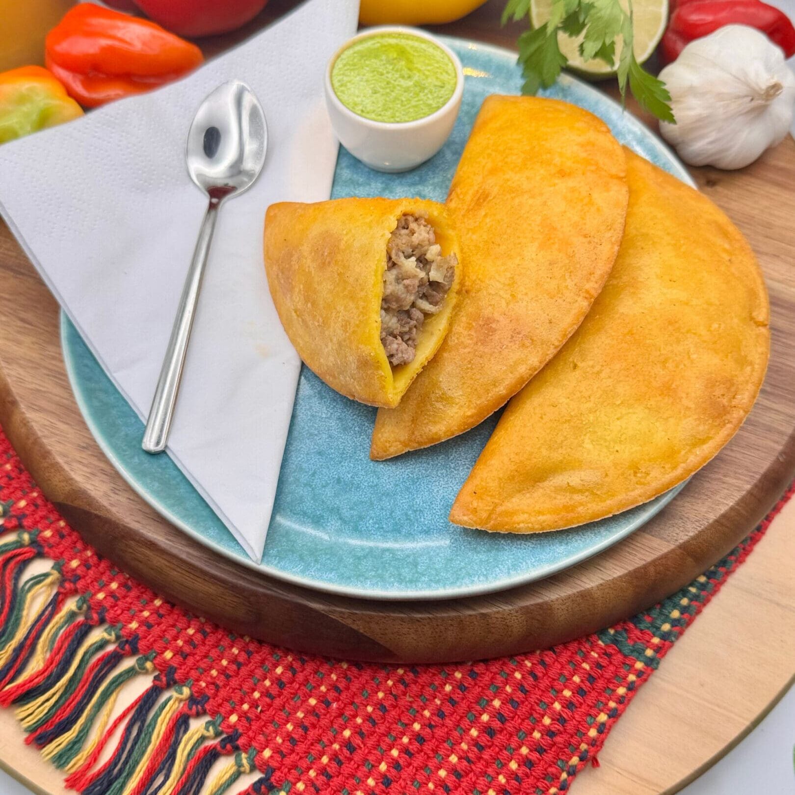 Two golden empanadas on a plate with dipping sauce and utensils.