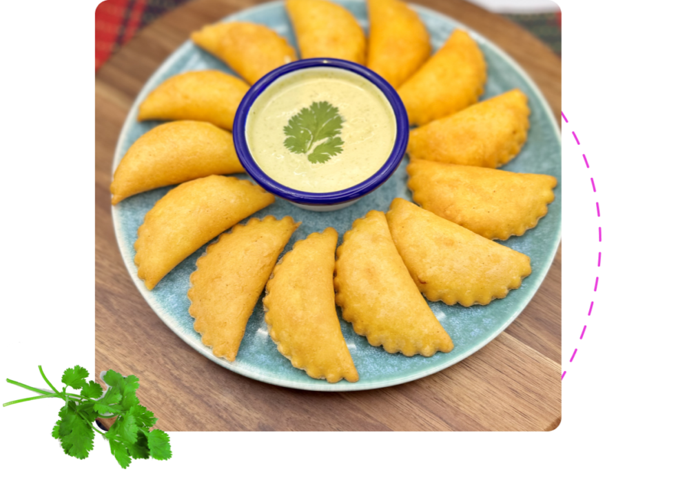 Plate of golden fried empanadas with dipping sauce in the centre.
