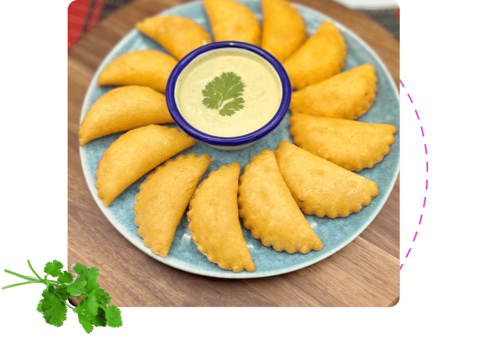 A platter of corn empanadas with a garlic salsa