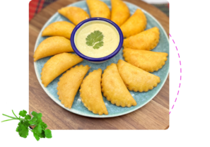 Plate of golden fried empanadas with dipping sauce in the centre.