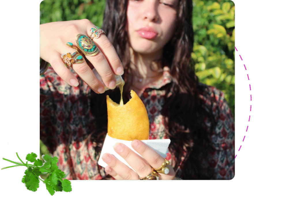 Person drizzling sauce over golden empanada held in hand outdoors