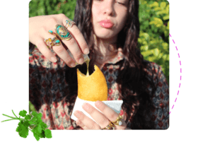 Person drizzling sauce over golden empanada held in hand outdoors