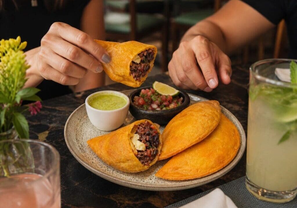 Hands reaching for plated golden empanadas with shredded beef, plantain and cheese - Illustrative Image